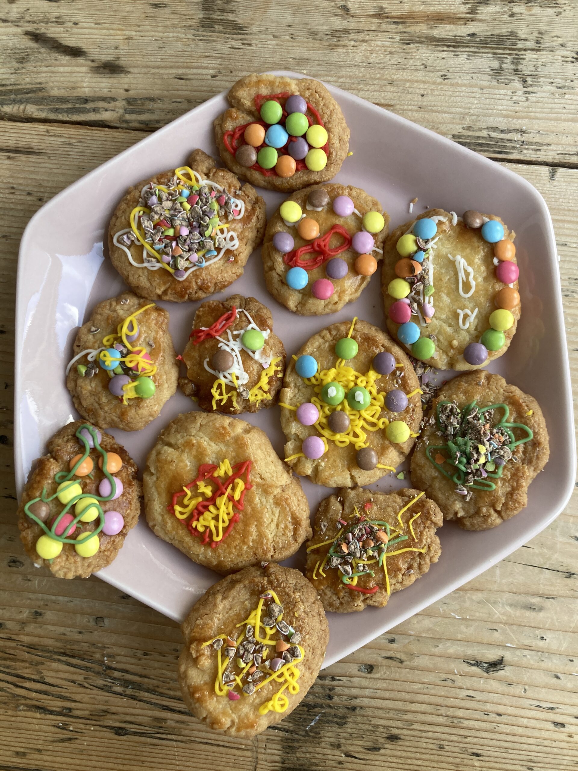 Zelf gebakken koekjes met kleurrijke versieringen op een pink bord.