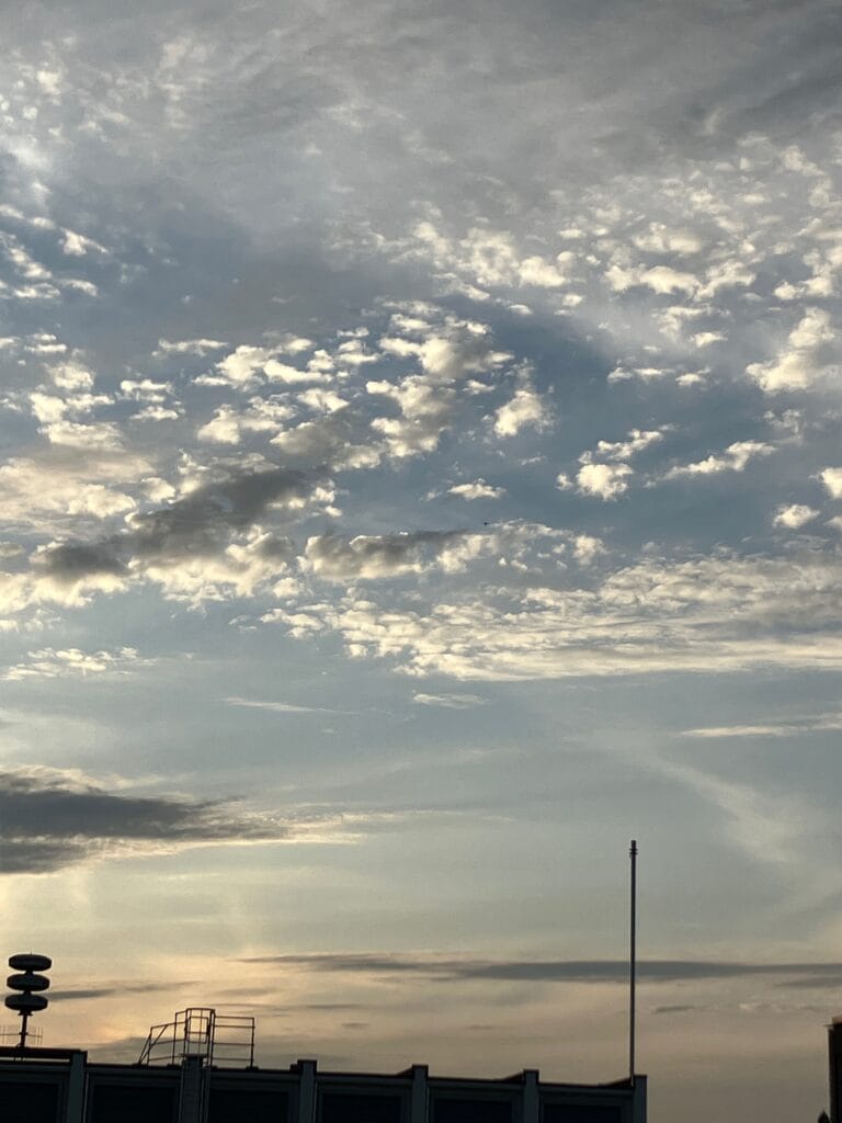 Avondhemel met witte wolkjes aan de kust. In de voorgrond rechts een dunne paal.